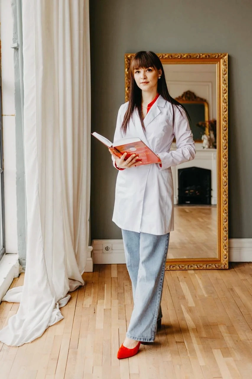 Специалист в белом халате стоит с открытой книгой в руках